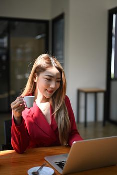 Thoughtful businesswoman drinking coffee and checking email on laptop computer.
