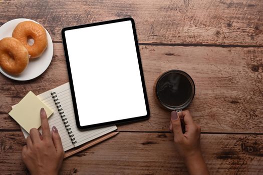 Young woman holding coffee cup and using digital tablet on wooden table.