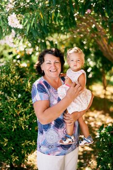 Woman holding a little girl in her arms near green tree. High quality photo