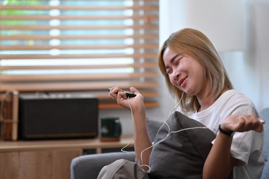 Cheerful asian woman sitting on sofa and listening music on earphone.