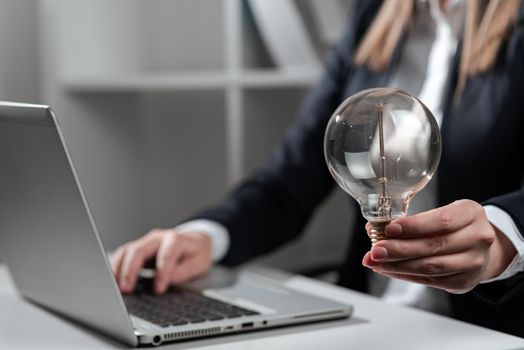 Businesswoman Typing Recent Updates On Lap Top On Desk Holding Lightbulb.