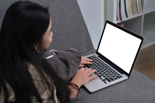 Asian girl lying on comfortable sofa and using laptop computer.
