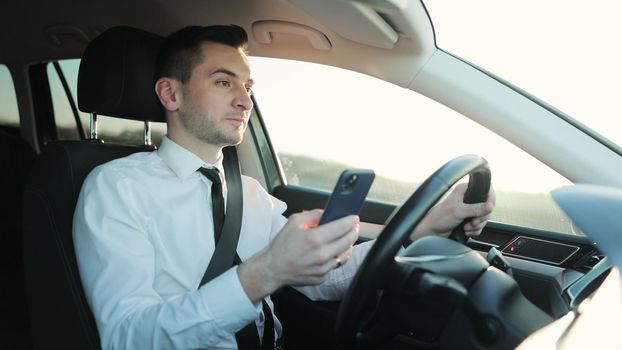 Concentrated man sitting at driver's seat in car and chatting. Businessman in Automobile. Concept, innovation, message, communication, holding, messaging.