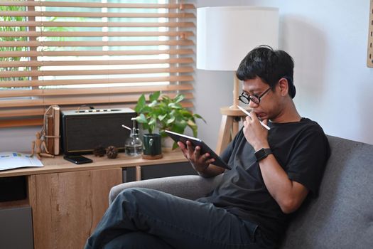 Man sitting on comfortable sofa and using digital tablet.