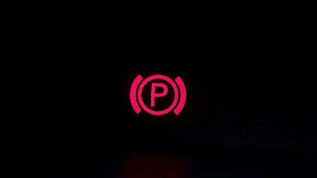 Parking brake control light in car dashboard. Close up of car's parking brake light coming on, on the dashboard.