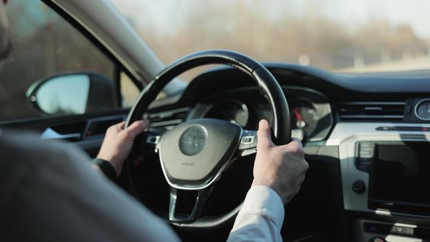 Man driving car with autopilot. Businessman in white shirt driving car. Driver's hand on the steering wheel against the background of the road. Elegant male driver traveling by automobile.