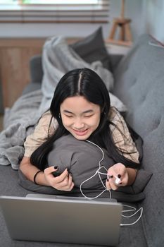 Happy young woman lying on sofa and using laptop computer.