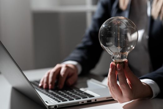 Businesswoman Typing Recent Updates On Lap Top On Desk Holding Lightbulb.