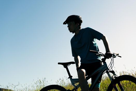 silhouette of a young man with his mountain bike in the countryside, concept of sport and healthy lifestyle in nature, copy space for text