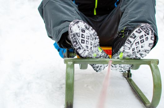 Winter holidays and games concept. The child is sitting on a sleigh. Close-up legs in the snow. Winter close-up