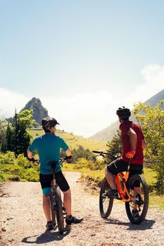 vertical photo of two young cyclists watching the path during a break in their mountain bike route, concept of sport with friends and healthy lifestyle in nature, copy space for text