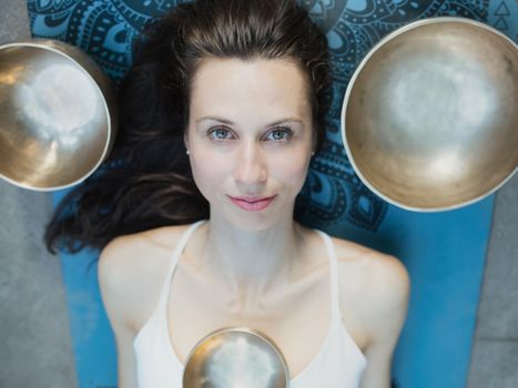 Yoga concept, meditation and sound therapy. Portrait of beautiful young caucasian woman surrounded by copper tibetan singing bowls and instruments.