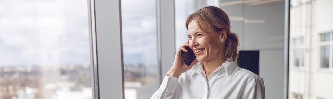 Portrait of middle aged woman using mobile phone and making a call while working at office.