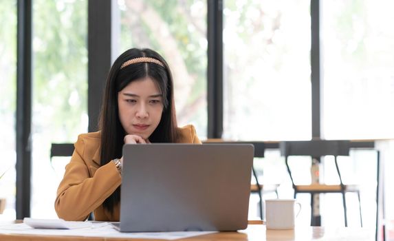 Young Asian woman working at office using a laptop computer on a table..
