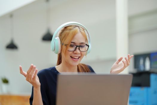 A portrait of a young Asian woman with blonde hair wearing over-ear headphones listening to music to relax while taking a break from boring day activities.