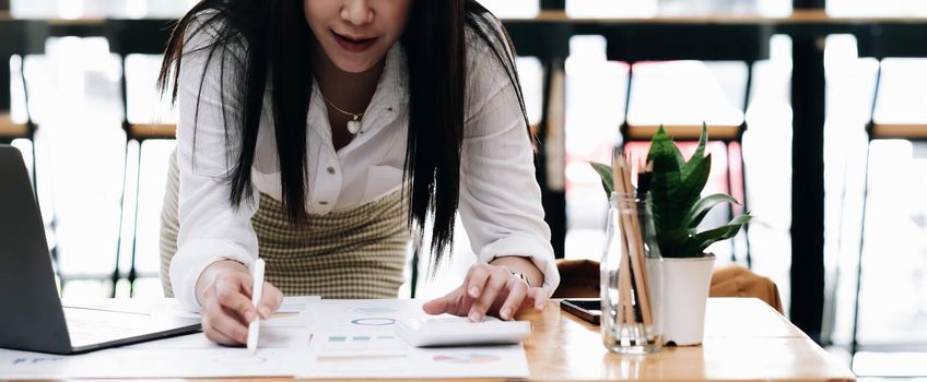 Close up of businesswoman or accountant hand holding pen working on calculator to calculate business data, accountancy document and laptop computer at office, business concept.