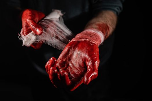 A man covered in blood bandages his hands