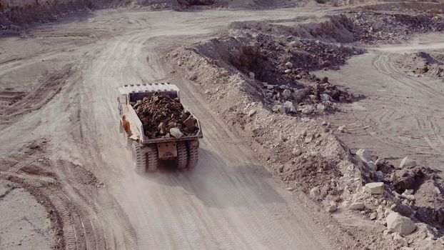Dump truck loaded with ore and driving through the pit. Big yellow heavy truck in open cast mine mining of coal the overall plan. Open pit anthracite mining, mining truck at work working in quarry.