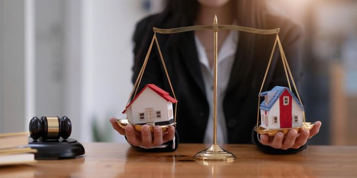 Female lawyer protecting a house model on a scales of justice. Property and legal concept. Houses Litigation. cropped image.