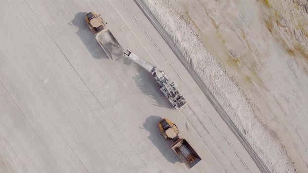 Aerial top down view of an excavator loading crushed stone into a dump truck in a crushed stone quarry. Mining industry. Heavy industry. The smart process in an iron ore quarry
