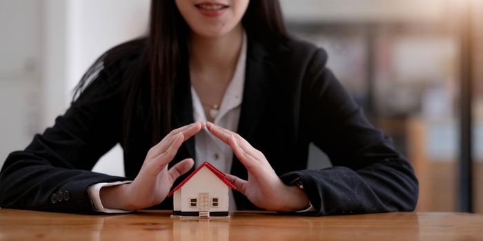 Home protection concept, close up of female hands sheltering modern house.