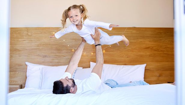 Adorable little girl bonding with her single father at home and pretending she can fly. Caucasian single parent holding and lifting his daughter in the air. Smiling child playing in the bedroom.