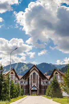 The main building with the hotel of the Ak Bulak mountain resort in the summer tourist season. Copy space, vertical. Almaty, Kazakhstan - June 19, 2021