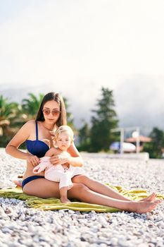 Mom in a bathing suit puts on a little girl a jumpsuit on the beach. High quality photo