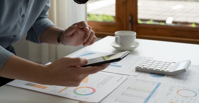 Cropped shot of businesswoman using mobile phone while working for financial count number in modern office.