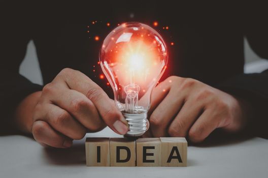 Text idea with a hand holding a light bulb Innovative wood cube block solution.