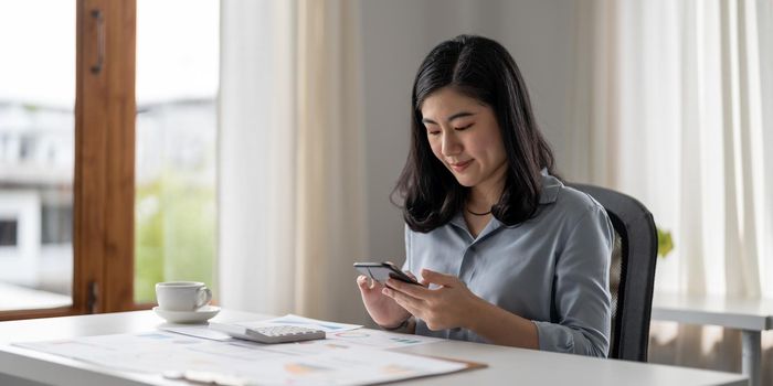 Business asian woman using mobile phone during checking an email or social media on internet. accounting financial concept