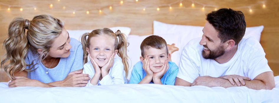 Happy carefree caucasian family lying cosy on bed while bonding together at home. Loving parents spending quality time with little son and daughter. Cute kids enjoying lazy morning with mom and dad.
