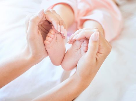 Mother holding baby feet. Closeup of tiny newborn baby feet held by a parent. Small baby toes. Little baby lying on a bed. Woman holding feet of little baby girl. Innocent infant being held by mother.