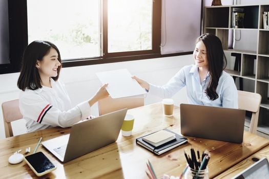 Two female company employees happily smiled at each other as they handed each other folders