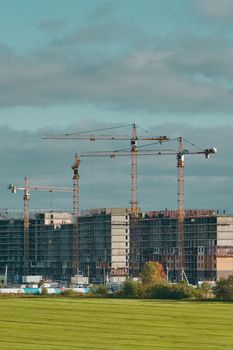 Construction site with industrial building cranes, multi-storey buildings of new city districts and large green field. Project of urban area. Blue sky with clouds.