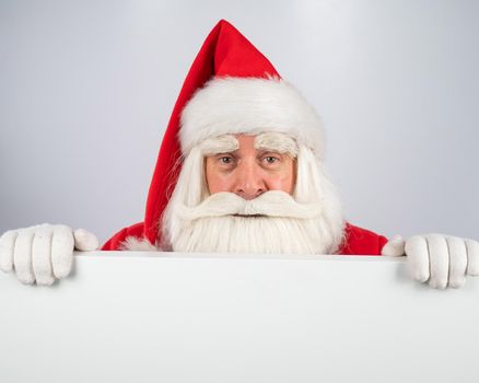 Santa Claus peeks out from behind an ad on a white background. Merry Christmas