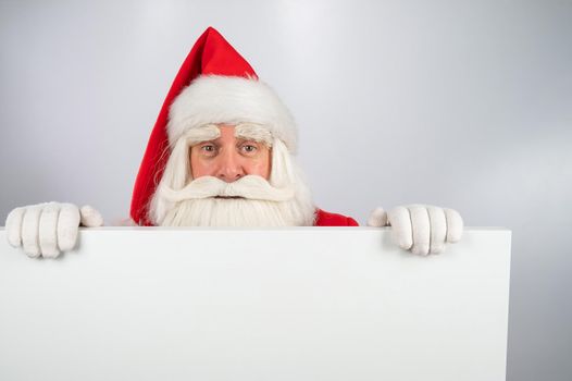 Santa Claus peeks out from behind an ad on a white background. Merry Christmas