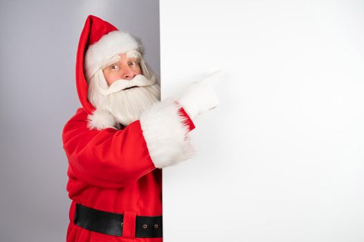 Santa Claus peeks out from behind an ad on a white background. Merry Christmas