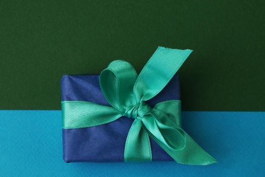 Blue gift box with a green bow on a double blue and green background.