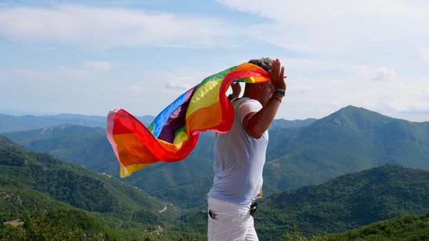 Bisexual, gay, old man, male, transsexual walk with LGBTQIA flag, rainbow peace in pride mounts on the nature on a day and celebrate Bisexuality Day or National Coming Out Day