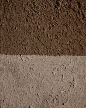 Close-up on a wall made of two-tone plaster. The wall is painted with dark brown and light brown paint.