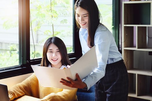 Two female company employees happily smiled at each other as they handed each other folders