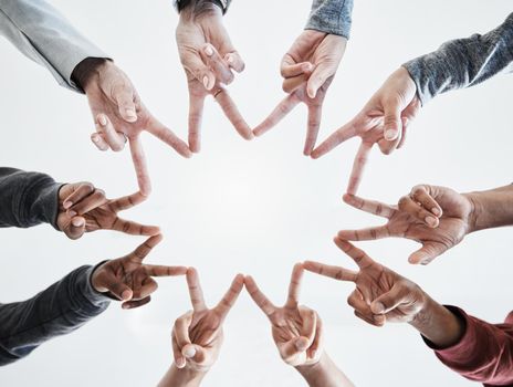 Below hands in circle making a star shape. A group of people putting their fingers together while standing in a huddle outside against a clear and bright sky. Anything is possible with teamwork.