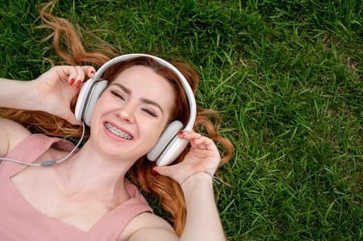 A young red-haired woman lies on the grass and listens to music