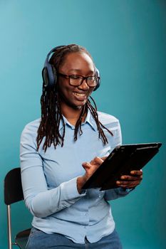 Confident smiling young lady having digital touchscreen tablet while listening to music playlist. Attractive person with wireless electronic portable device listening to podcast while surfing web.