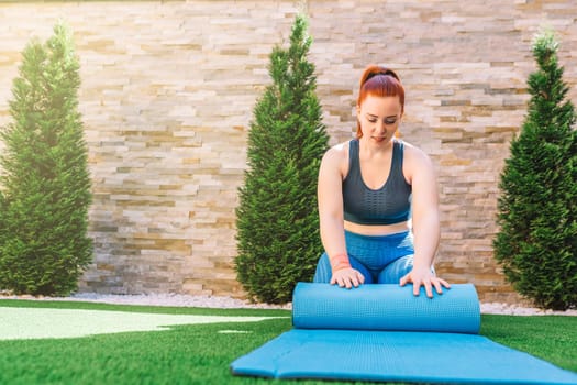 Young woman and beautiful sportswoman training, stretching a yoga mat to practice stretching exercises at sunrise. girl doing sports exercises at home. concept of health and wellness. natural light in the garden.