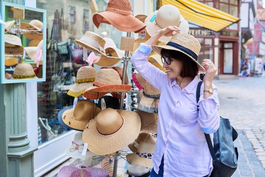Woman tourist choosing to buy a straw hat in a store. Fashion, style, summer, holidays, shopping concept