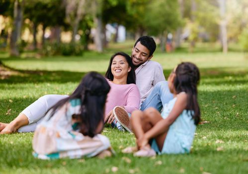 Portrait of happy asian couple lying together on grass. Kids playing while watching their loving parents spending time together at the park.