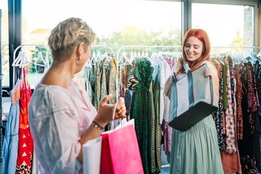 two friends enjoying and shopping in a clothes shop, taking pictures with their mobile phone. mother and daughter enjoying a shopping day together. shopping concept. natural light from window.