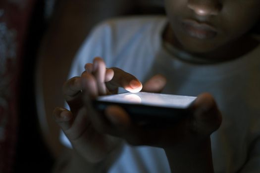 teenage boy sitting on sofa using smart phone at night .